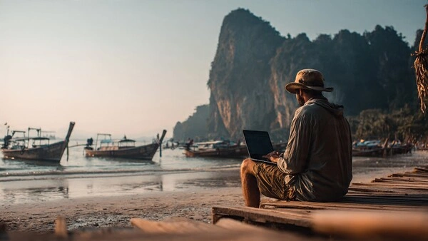 La mentira del nómada digital: lo que nadie te cuenta antes de lanzarte (2026) Persona sentada frente al mar con un portátil, reflexionando sobre el trabajo remoto y la idea de ser nómada digital antes de tomar la decisión de viajar
